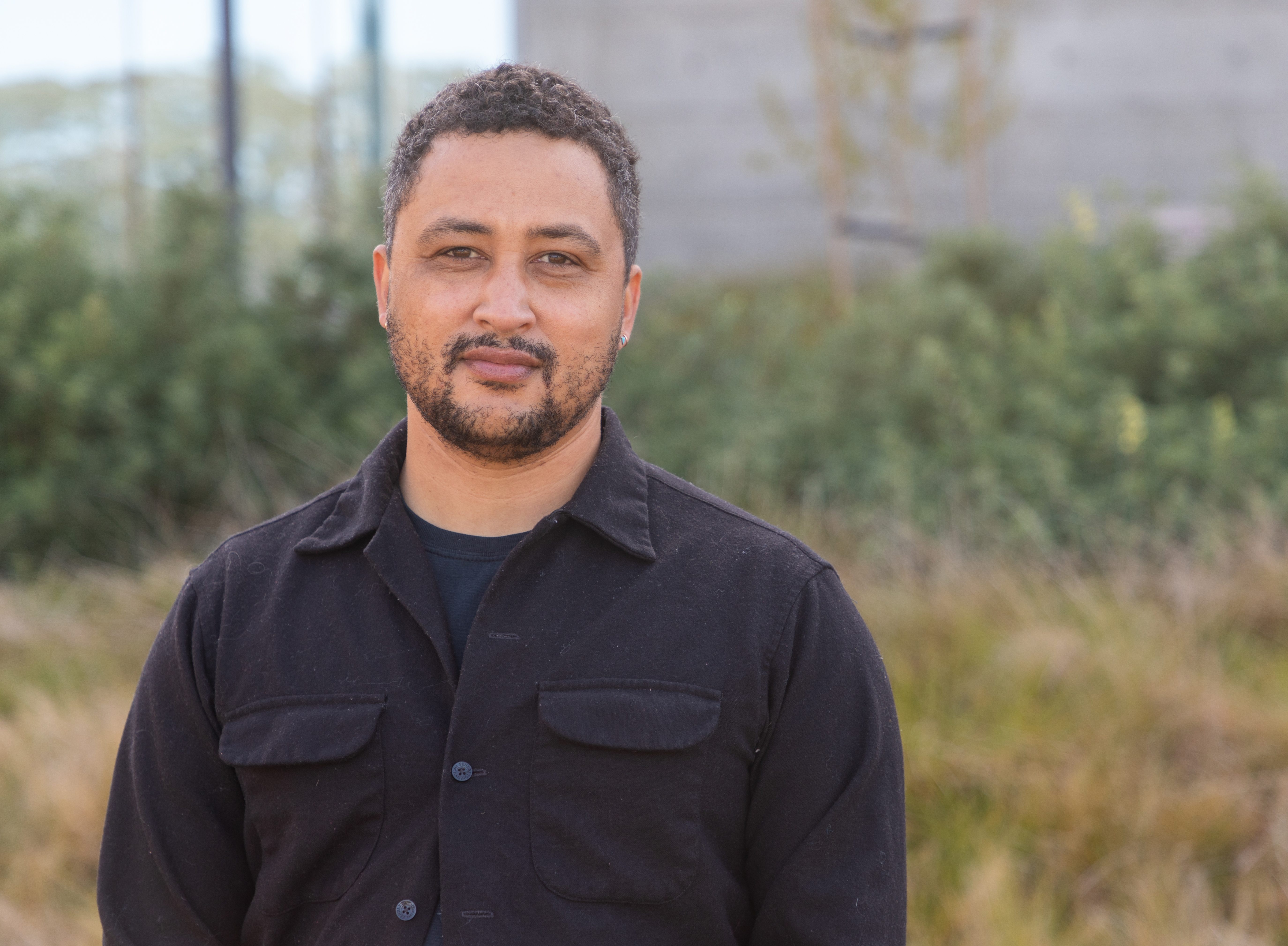 A man standing in front of a hill. We see him from the bottom of his sternum to the top of his head.