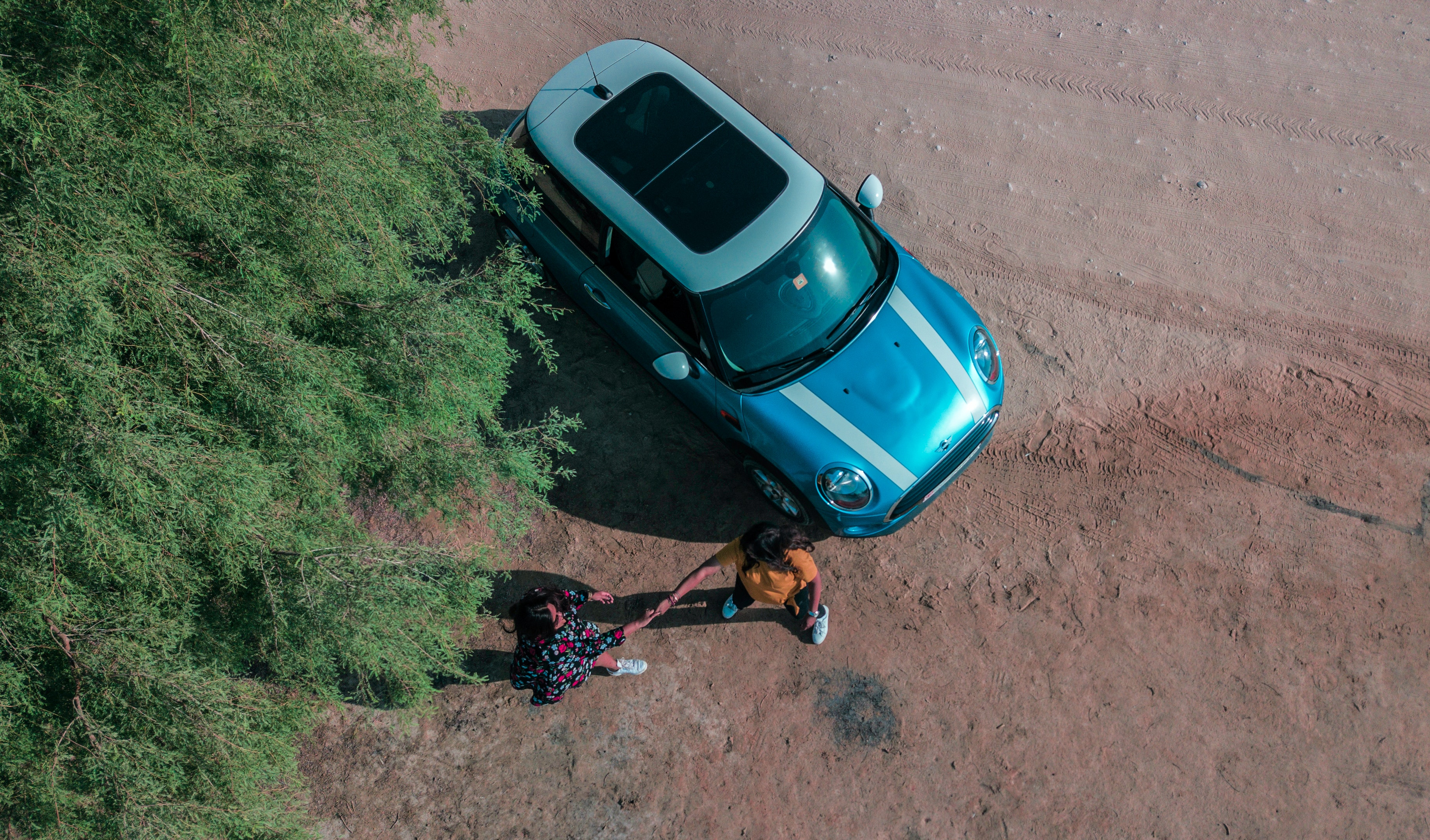We have a top-down view of two woman greeting each other near a car as if we were floating over them.