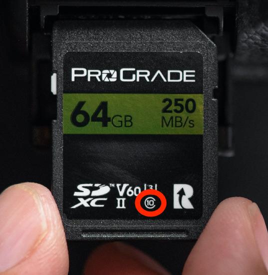 Fingers holding SD card. The number 10 inside the letter C is circled in red.