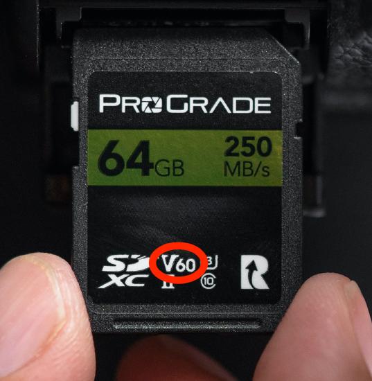Fingers holding and SD card. V60 is circled in red.