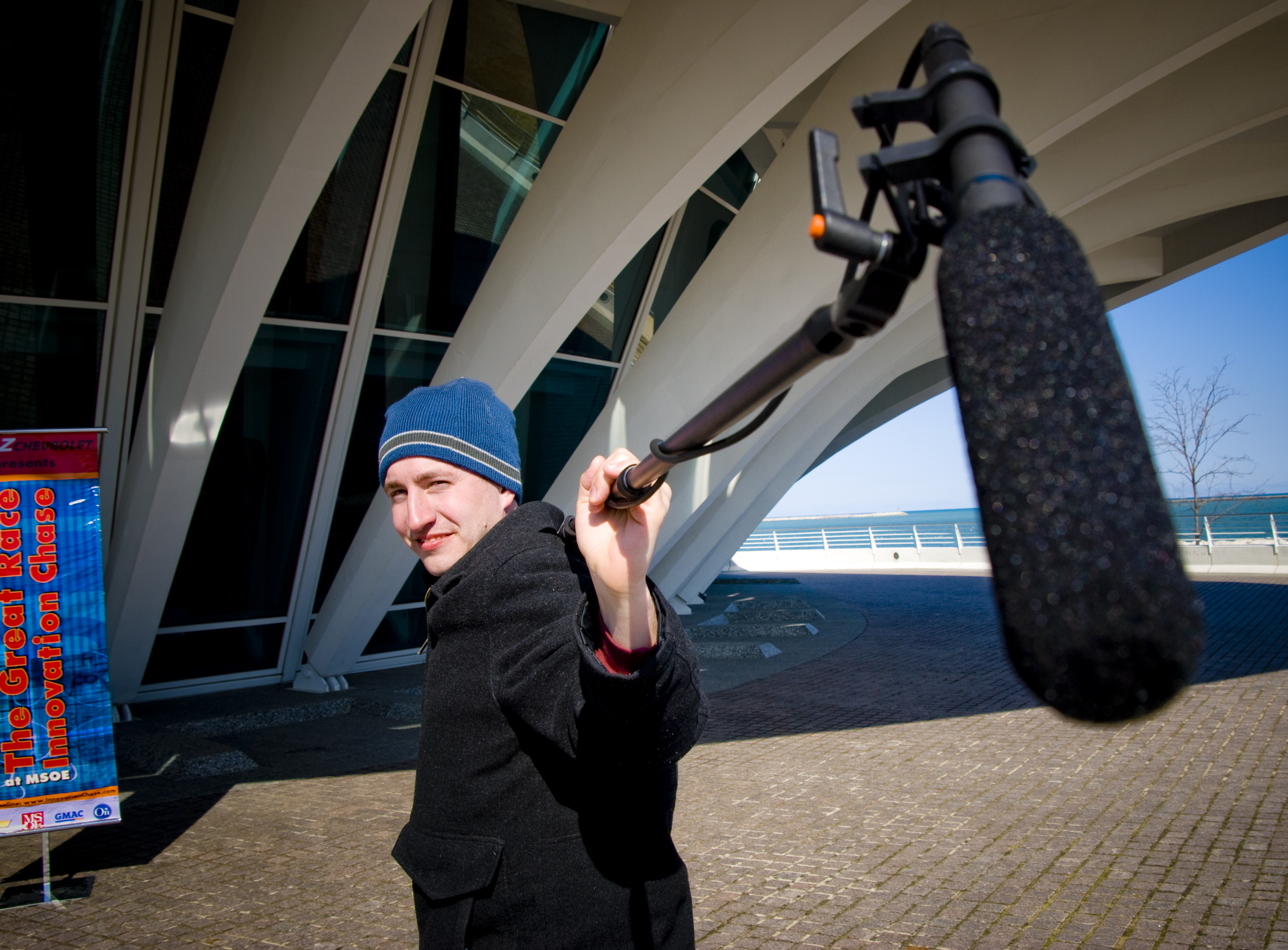 Man holding a boom mic on his shoulder pointing toward the viewer.
