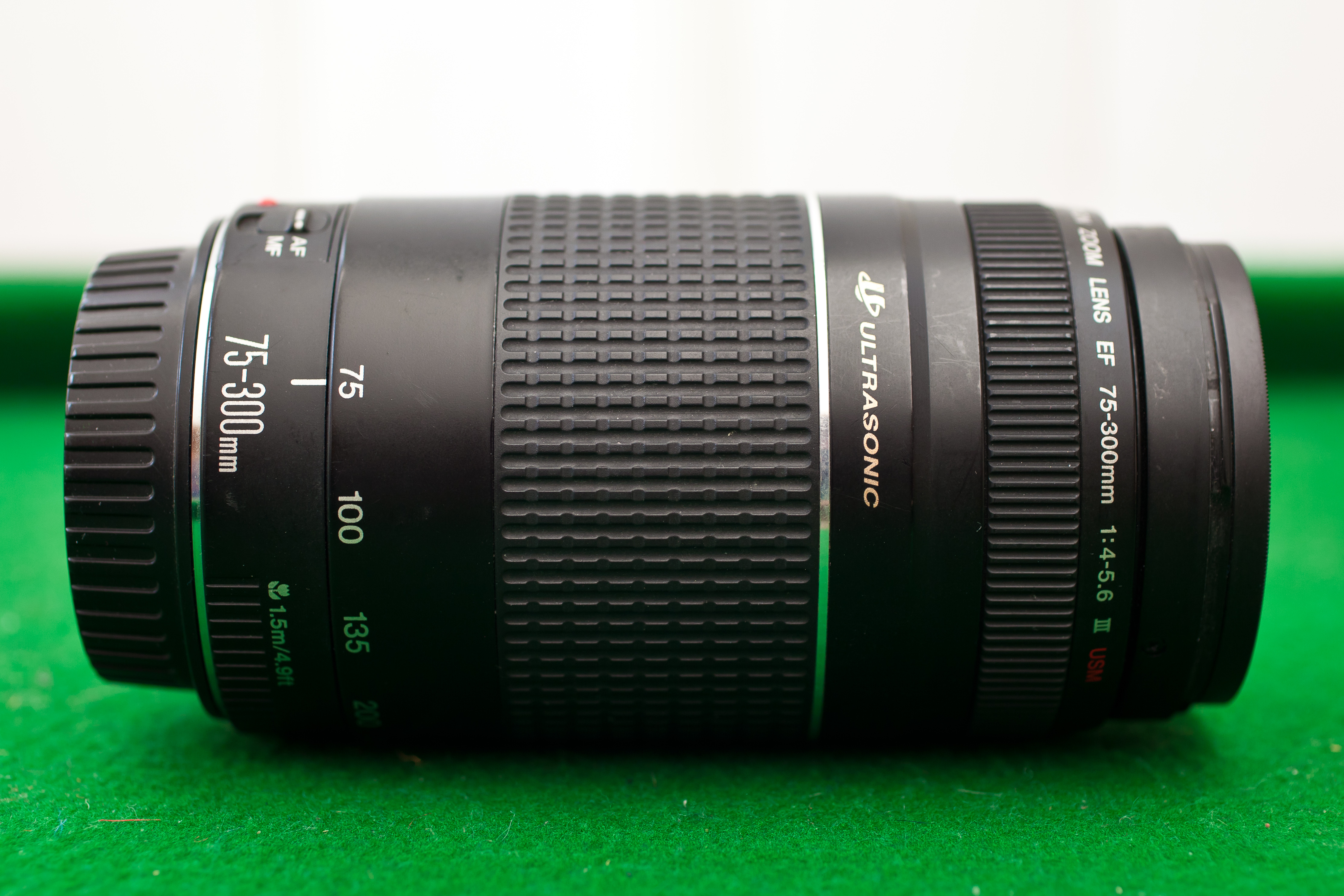 A 75mm to 300mm lens laid on its side on green felt.
