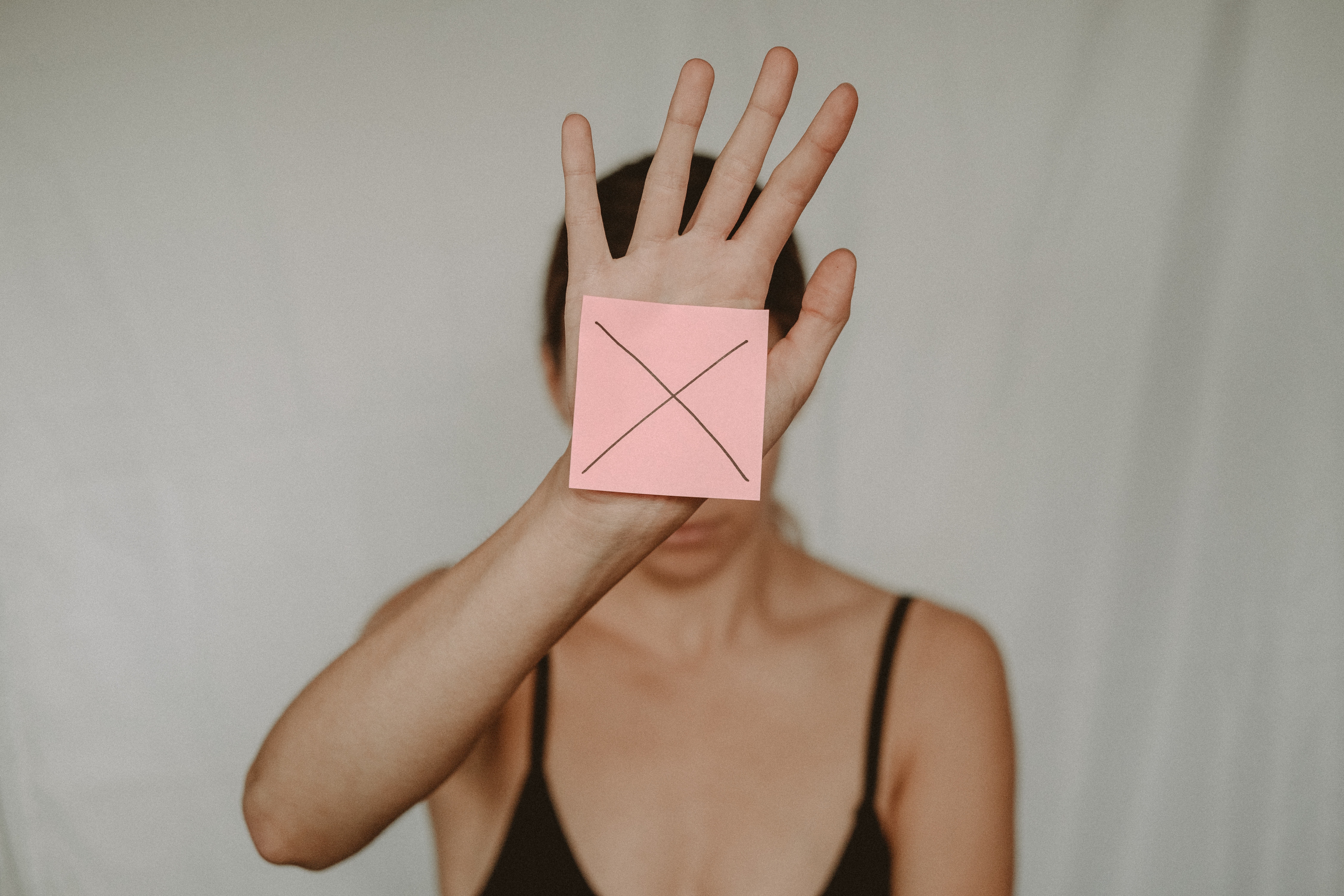 Una mujer sostiene una nota post-it con una X en ella frente a su cara.