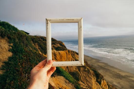 A hand holds an empty frame focusing our eyes on a particular part of a bluff and ocean view.