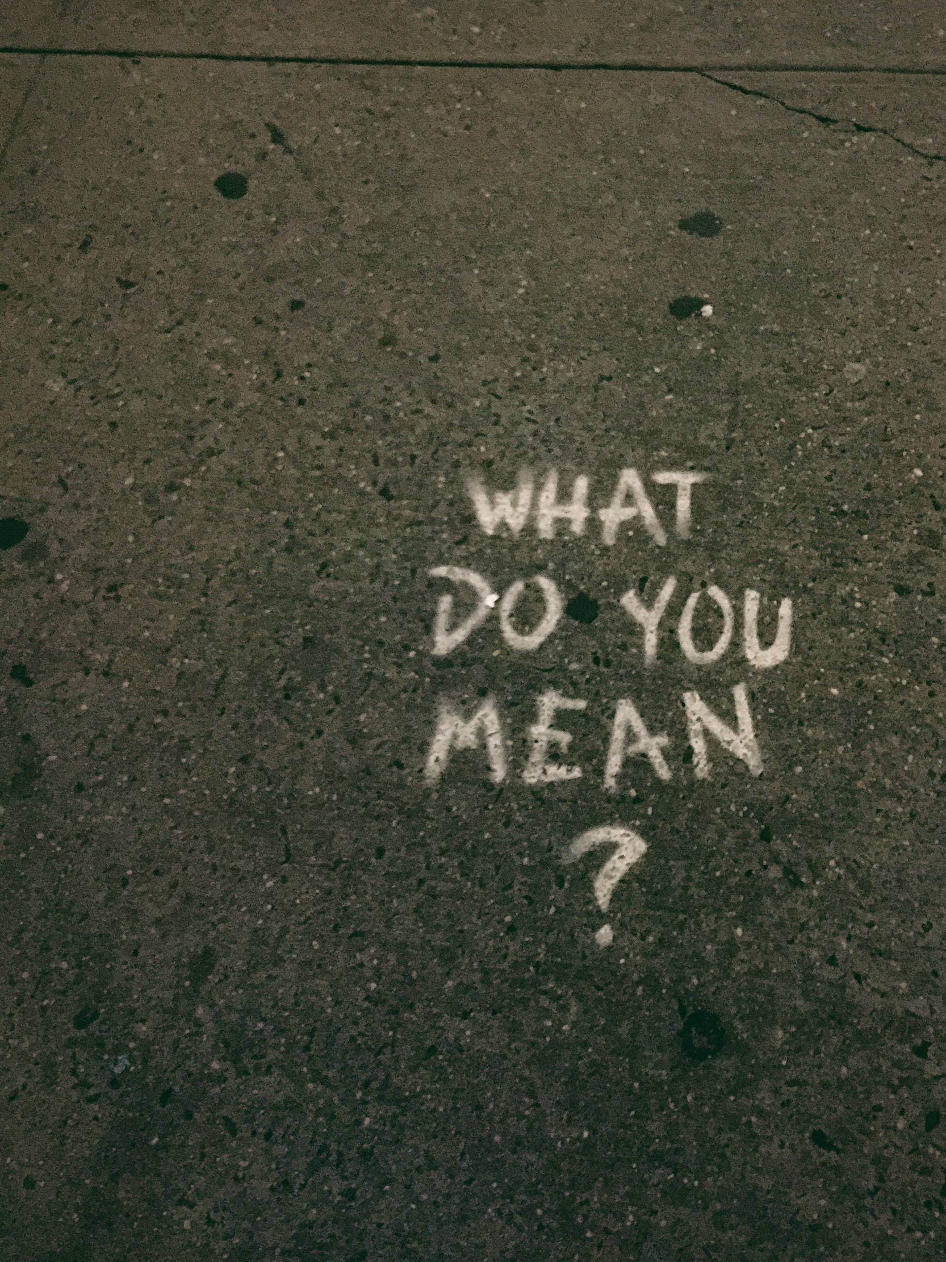 The words "What do you mean?" written in chalk on pavement.