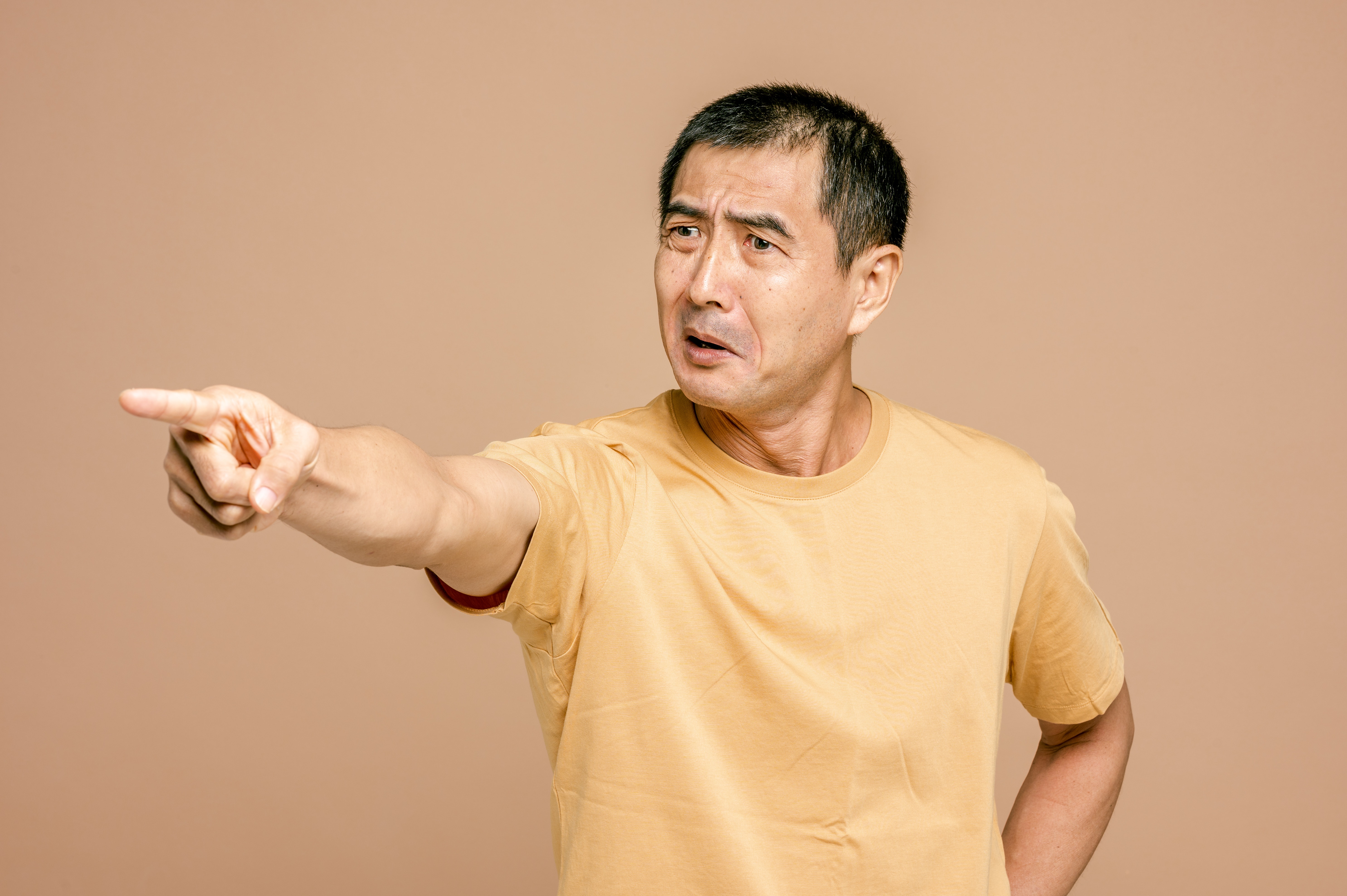 एक बूढ़ा एशियाई आदमी एक उंगली को सीधे बाहर की ओर इशारा करता है, जो चकित और घृणित दिखता है।
