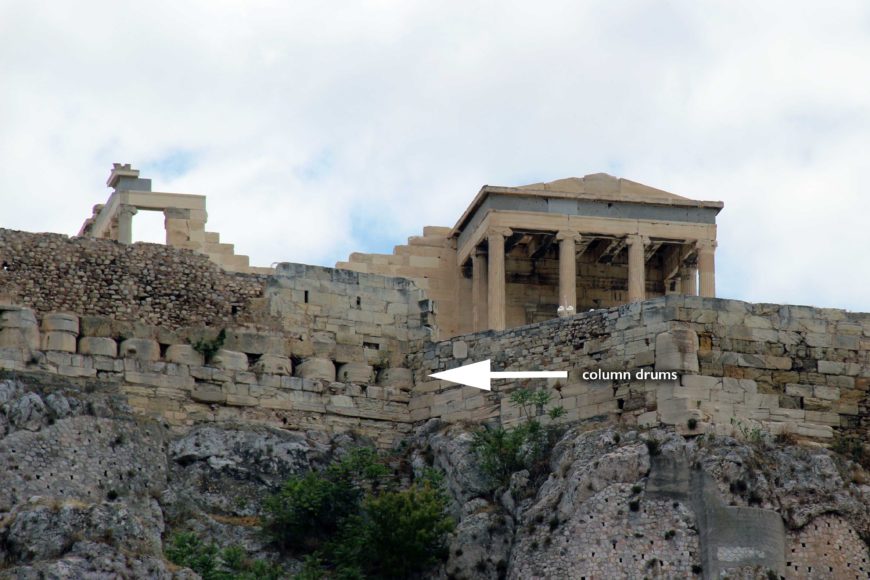 Залишки матеріалів з храмів, зруйнованих під час перського мішка Акрополя, такі як колонна-барабани (тут) і тригліф-метоп фриз, були включені в Північну стіну Акрополя.