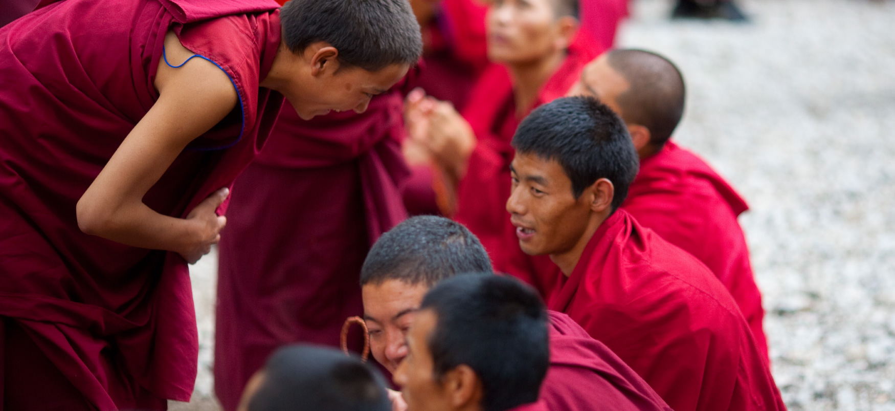 Monge budista em roupas vermelhas se curva para falar com outros monges em roupas vermelhas.