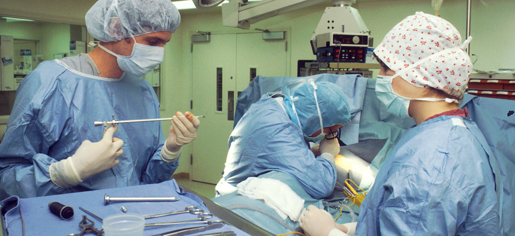 Trois professionnels de santé équipés d'équipements de protection individuelle préparent des instruments dans une salle d'opération.