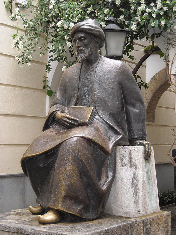 Estatua de un hombre sentado con una túnica larga y sosteniendo un libro en su regazo.