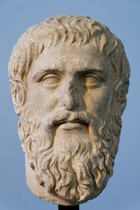 Скульптурний бюст чоловічого обличчя з густими волохатими волоссям і довгою кучерявою бородою.