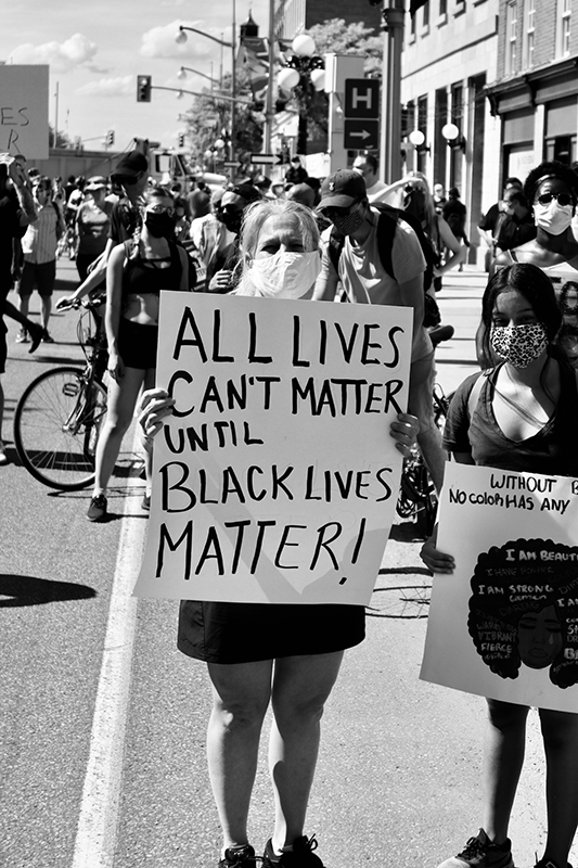 Жінка стоїть на вулиці, тримаючи плакат із написом «Все життя не може мати значення, поки чорне життя не має значення».