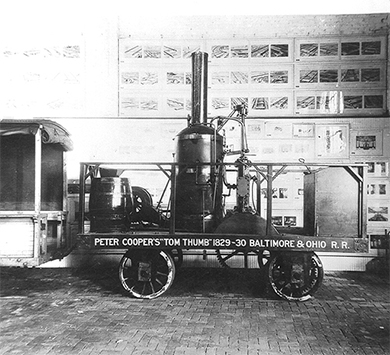 Une photographie d'une réplique de la locomotive à vapeur Tom Thumb est présentée. Sur son côté sont peints les mots « Tom Thumb » de Peter Cooper, 1829-1830, Baltimore et Ohio R.R. »