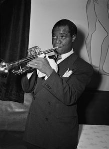 Black and white photographic image of Louis Armstrong playing the trumpet.