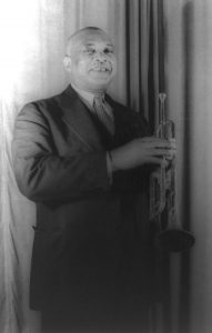 Black and white photographic image of W.C. Handy standing in a suit holding a trumpet.