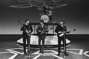 Black and white photographic image of the Beatles playing live.