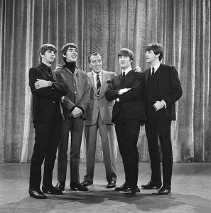 Black and white photographic image of the Beatles standing with Ed Sullivan.