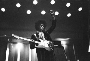 Black and white photo of Jimi Hendrix playing guitar live at a venue.