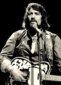 Black and white photograph of Waylon Jennings performing at a show live (1976)