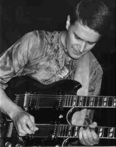 Black and white photo of John McLaughlin playing a double necked guitar