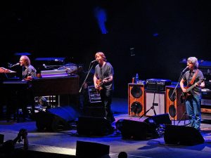 Color photo of Phish live with blue lights in the background.