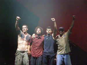 Color photo of Rage Against the Machine. Three of the four members are raising their fists.