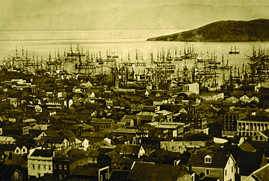 Una fotografía muestra una vista aérea del puerto de San Francisco. Las calles están abarrotadas de casas, y el agua llena de barcos.