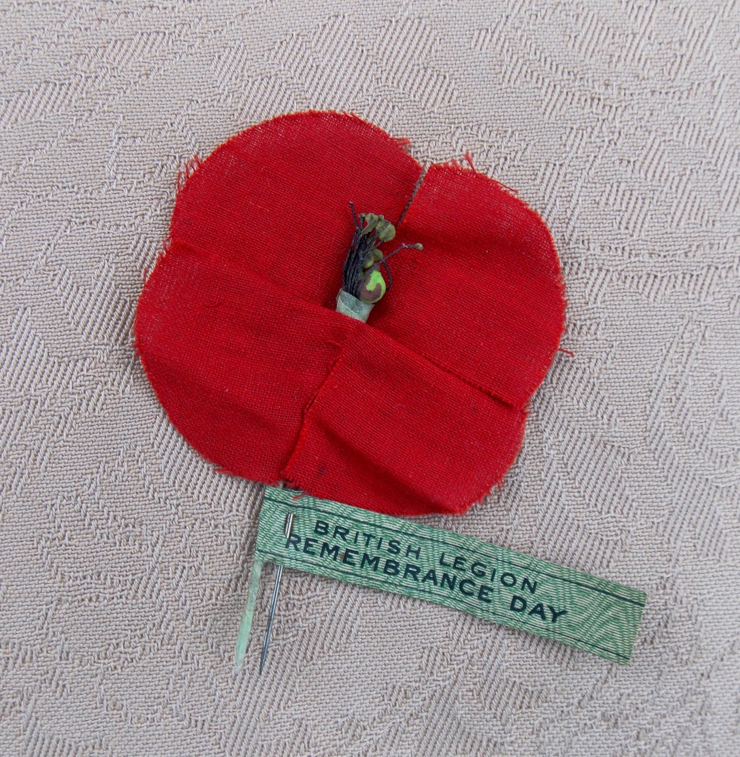 Photo of a hand sewn red poppy with the words 'British Legion Remembrance Day' on the stem.